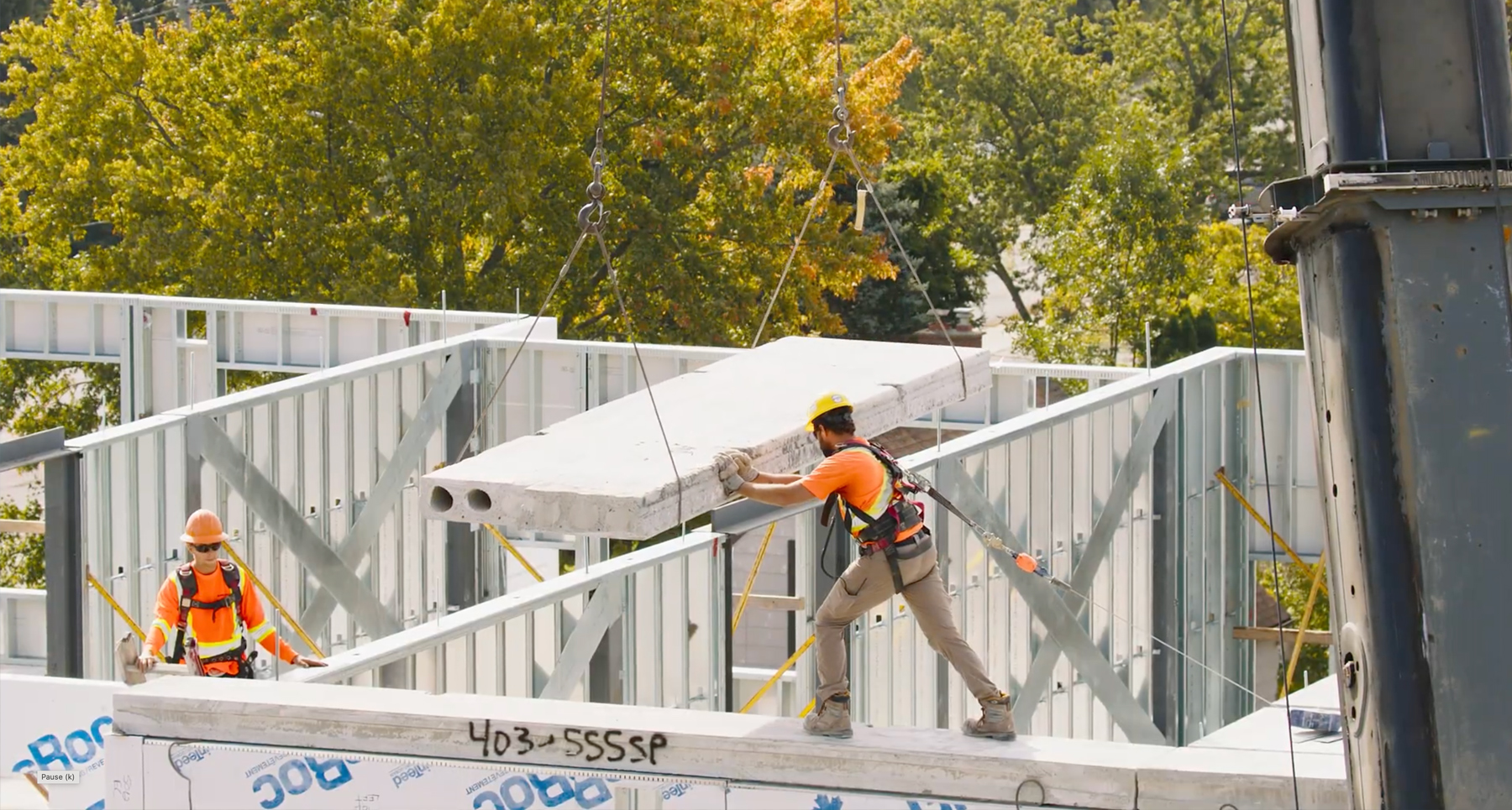 Construction worker on a building rooftop set a large concrete block being hoisted by a crane.